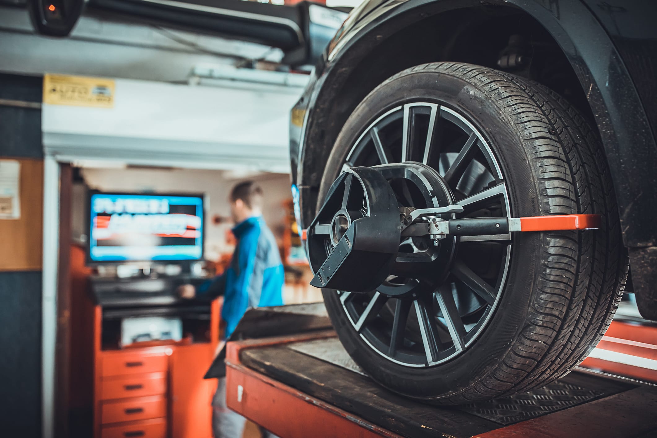 One man, mechanic in auto repair shop, wheel alignment equipment on a car wheel in a repair station.
